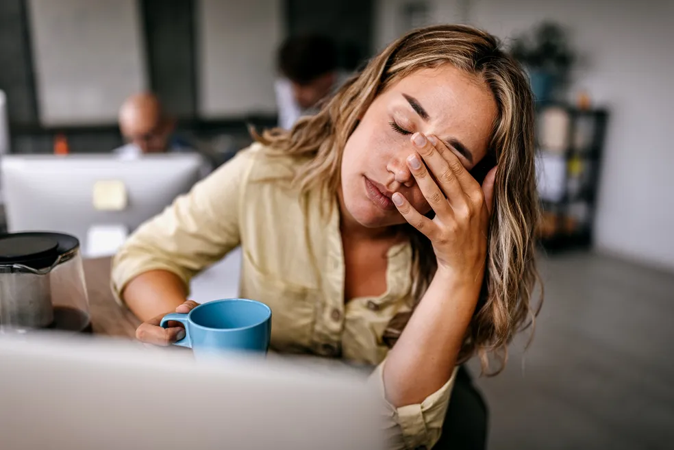 Mulher cansada no escritório segurando uma xícara